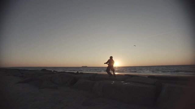Male dancer performs fiercely on jetty in front of ocean, wide angle steadicam pulls back