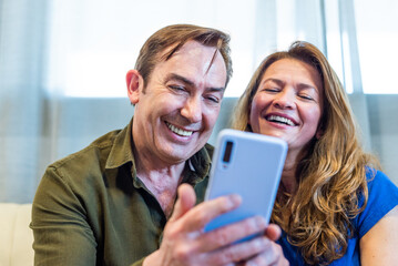 Smiling mature couple at home watching something funny on mobile.