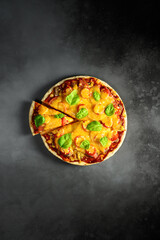 Top view of hot tasty homemade pizza with green basil leaves on the dark grey concrete background. Italian pizza on the black slate tabletop. With copy space for text. Flat lay
