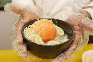 chief holding a bowl of portioned raw salmon fillets in ice with lemon.