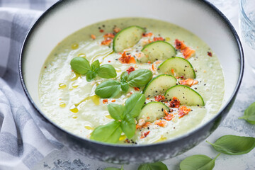 Closeup of a grey bowl with cold gazpacho made of cucumbers and green basil, selective focus, studio shot