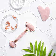 Pink Quarts stone face roller and serum capsules in round glass dish and hexagons. Gua sha stone...