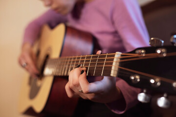 Obraz premium A young girl at home is learning to play the guitar, the brother showed her the chords and she clamps the strings and play the melody, focus on the fingers and guitar strings