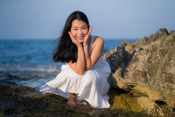 young happy and beautiful Asian woman by the sea - Attractive Chinese girl in white dress enjoying relaxed summer holidays at tropical island in travel and lifestyle concept