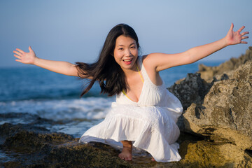 Fototapeta na wymiar young happy and beautiful Asian woman by the sea - Attractive Chinese girl in white dress enjoying relaxed summer holidays at tropical island in travel and lifestyle concept