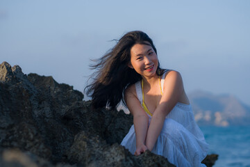 Fototapeta na wymiar young happy and beautiful Asian woman by the sea - Attractive Japanese girl in white dress enjoying relaxed summer holidays at tropical island in travel and lifestyle concept