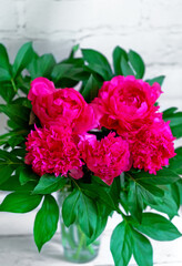 Five bright pink peonies stand in a glass vase on the table. Flower delivery all year round