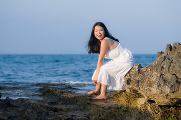 Fototapeta na wymiar young happy and beautiful Asian woman by the sea - Attractive Korean girl in white dress enjoying relaxed summer holidays at tropical island in travel and lifestyle concept
