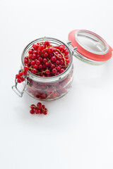 Handful of red currants in an open glass jar on a white background