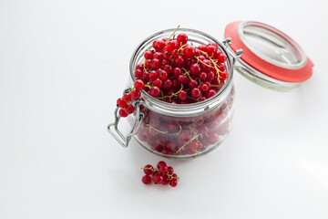 Handful of red currants in an open glass jar on a white background