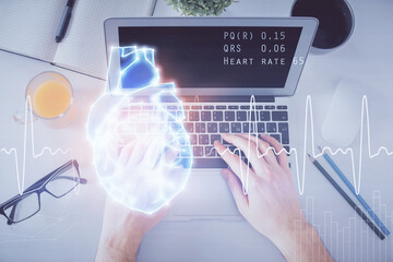 Double exposure of man's hands typing over computer keyboard and human heart hologram drawing. Top view. Medical education concept.