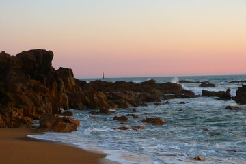 rocher dans la mer sur fond de coucher soleil, avec un phare au fond