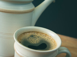 A cup of coffee, in a white cup on wooden table, blurred background, close up