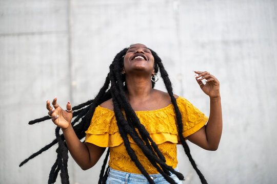 Beautiful young woman dancing in front of gray wall 
