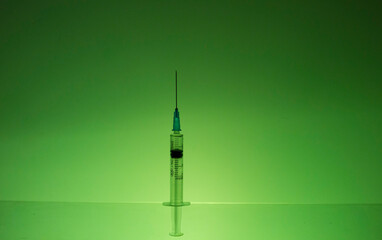A syringe with medicine stands against the green wall.