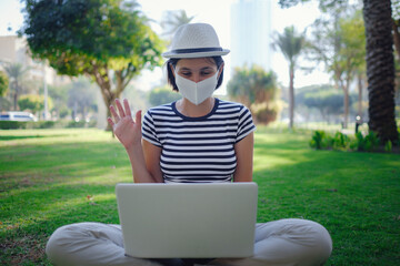 A woman is sitting on the grass in the park, working on her laptop.
