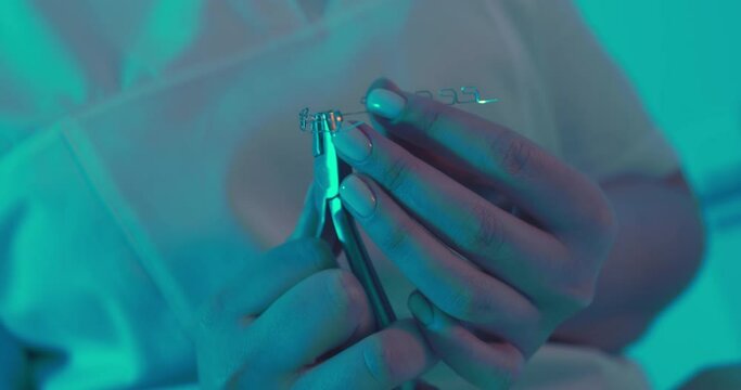 Close-up multiloop edgewise archwire is holding in the hand a female orthodontist and by using dental forceps is clenching it and then put to the ceramic model of teeth.