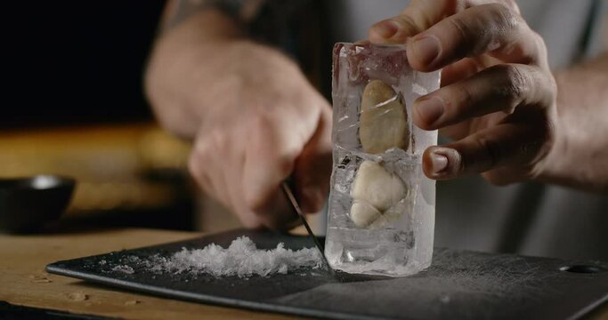 Bartender makes crushed ice from large ice cube by sharp knife, making the cocktail on the bar counter, refreshing cold drinks, 4k Prores HQ 120fps