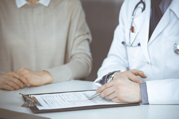 Unknown male doctor and patient woman discussing something while sitting in clinic and using clipboard. Best medical service in hospital, medicine, pandemic stop