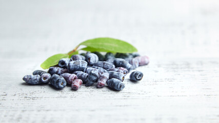 Honeyberry or haskap berries with fresh green leaves on grey wooden background