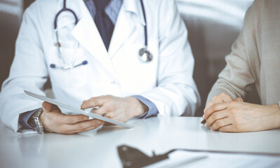 Unknown male doctor and patient woman discussing something while sitting in clinic and using tablet computer. Best medical service in hospital, medicine, pandemic stop