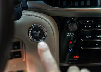 Obraz na płótnie Canvas Finger pressing button the start button, stop the engine in the luxury car. The man's finger is pressing down. Owner and dealership concept