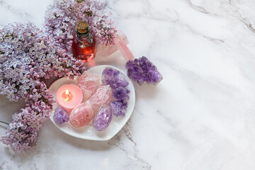 gemstones minerals, essential oil bottle, candle, lilac flowers on marble background. Crystal...