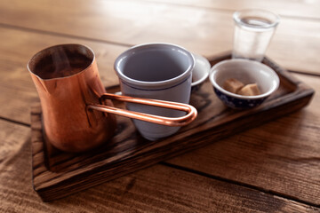 Tray with a cup, a copper Turk, sugar and cookies on a wooden table.
