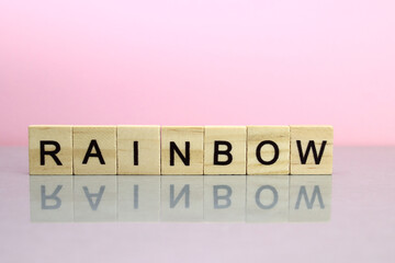 Rainbow word made of wooden letters on a pink background