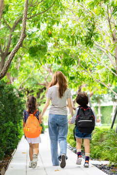 Parent and pupil of primary school go hand in hand. Woman and kids with backpack behind the back. Beginning of lessons.first day at school.Mother taking daughter to school