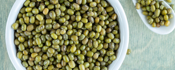 banner with top view on beans of mung sin white plate with spoon. close up mung on a green wooden background.