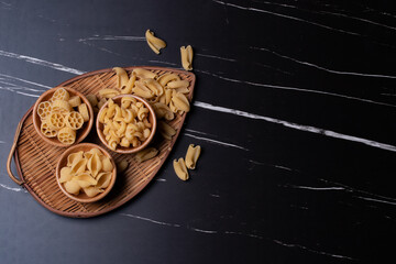 Raw pasta in a wooden cup on black marble background.Copy space