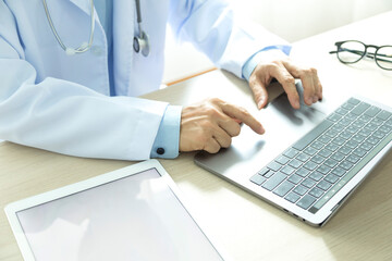 Doctor working and searching information about Patient database through internet laptop computer, tablet and have Stethoscope on his neck.