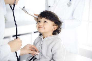 Woman-doctor examining a child patient by stethoscope. Cute arab toddler at physician appointment....