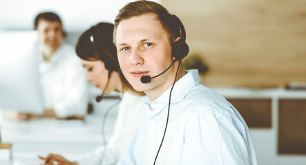 Group of diverse operators at work in call center. Businessman sitting n headset at customer service office. Business concept
