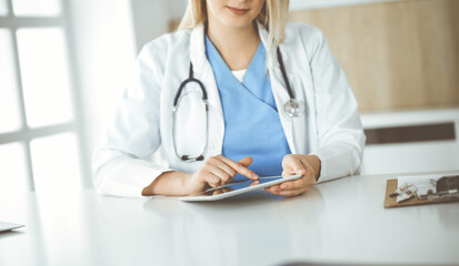 Unknown woman-doctor standing in clinic and using tablet pc, close-up. Data and best service in medicine and healthcare
