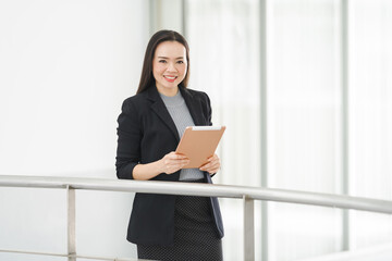 Portrait of a cheerful confident Asian businesswoman in a business suit standing whie using a digital tablet in the business building. Business stock photo