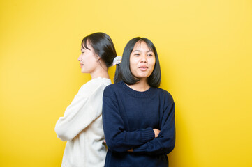 Young brunette standing with hands crossed and laughing wide on yellow background.