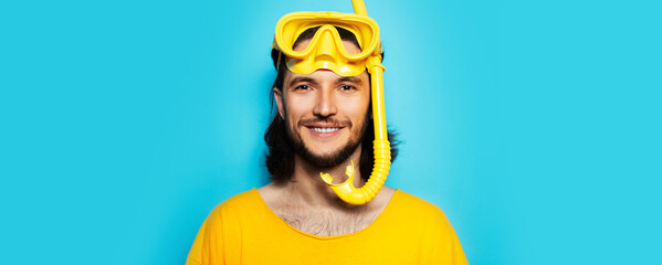 Young smiling man in yellow, wearing diving mask and snorkel on blue background.
