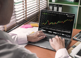 Business man investment Trading working on Laptop Stock market exchange information and Trading graph. Successful and young man in his office in front of computer screens with trading charts. 