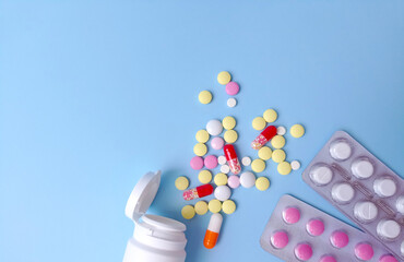 Colored tablets in bulk and in blisters on a blue background flat lay. Medicine, pharmaceuticals concept. Stock photography with copy space, selective focus. 