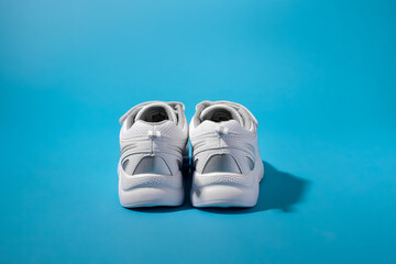 rear view of two backs or heels of white sneakers for children with silver inserts on a blue paper background with hard shadows.