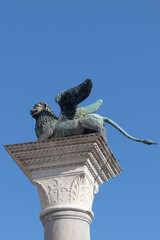 Bronze lion on the Piazza San Marco on blue sky background, Venice, Italy. Winged lion is a symbol of Venice. Ancient statue on a pillar close-up in Venice center