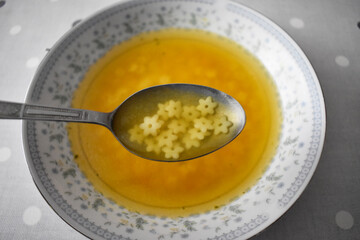 Hot bowl of chicken soup and spoon with soup and flowers noodles