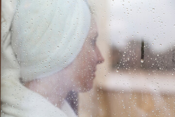 A middle-aged woman lying on the sun lounger on the terrace and rest in the fresh air after a hot bath, selective focus through fogged glass