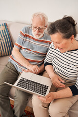Mature couple holding laptop and looking at the screen and discussing something