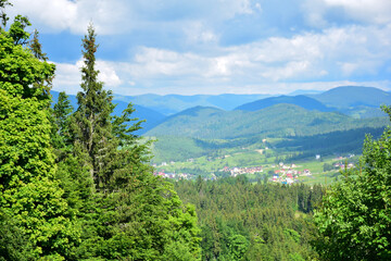 Fototapeta na wymiar Scenic view from the mountain to the village between the mountains covered with forest. View from afar