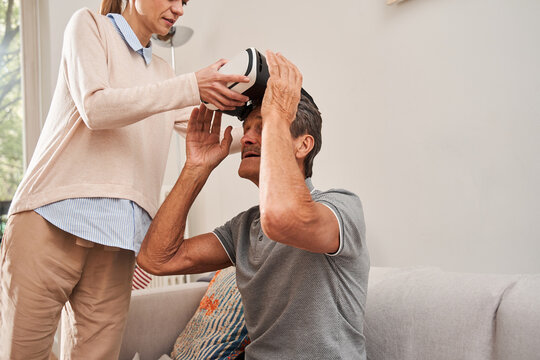 Happy young caregiver putting on senior man vr glasses