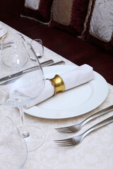 Festive table setting.A tablecloth with a textured pattern.Cotton napkin with a ring made of yellow metal.The concept of holidays.Wine glasses on the table.White plates. VIP lounge.Part of the