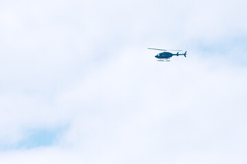 Blue helicopter flying in a white, cloudy and sunny sky